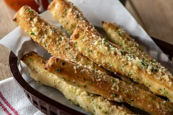 Crazy Bread sticks dusted with parmesan in a lined basket