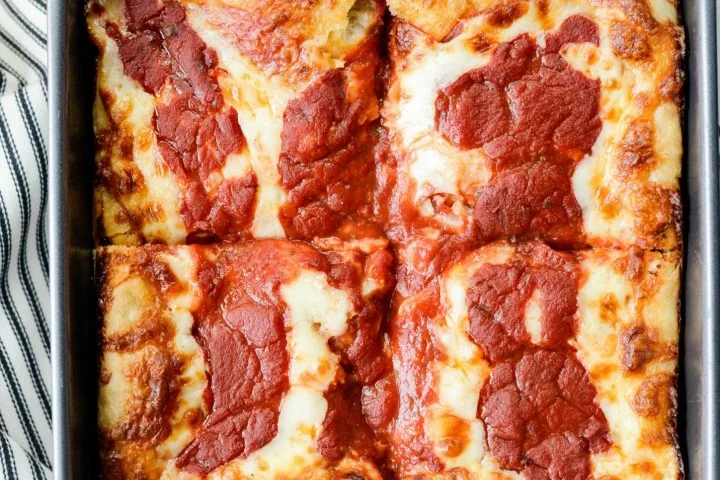 Detroit-style deep dish pizza in a steel pan with crispy caramelized cheese edges