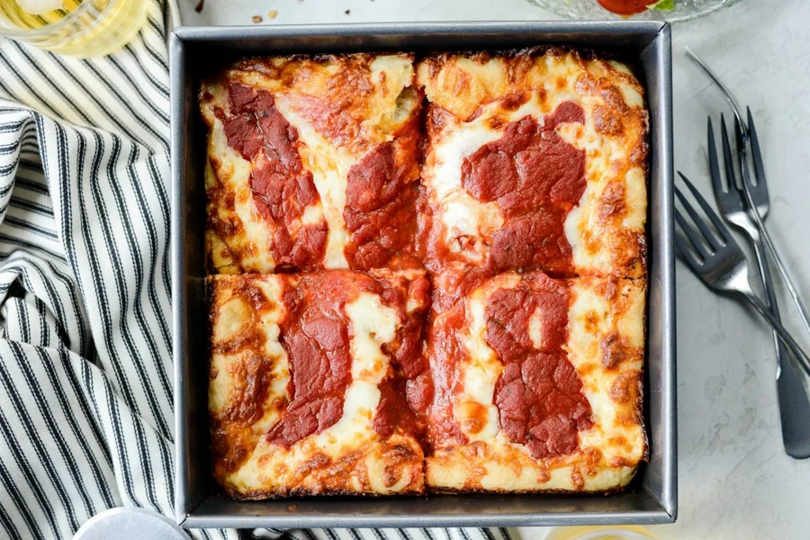 Detroit-style deep dish pepperoni pizza in a steel pan with crispy cheese edges