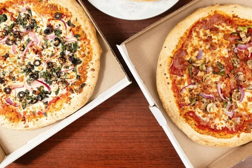 Two pizzas side by side on the counter, one pepperoni and one loaded with vegetables